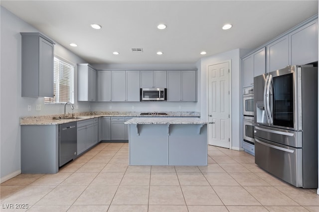 kitchen featuring gray cabinetry, light stone countertops, light tile patterned flooring, stainless steel appliances, and a sink