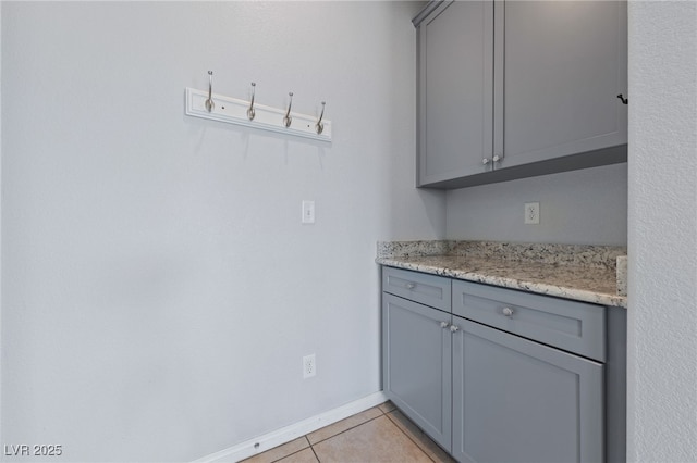 kitchen featuring light tile patterned floors, gray cabinets, baseboards, and light stone counters