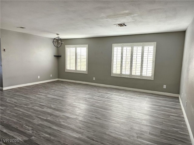 empty room featuring visible vents, dark wood finished floors, a notable chandelier, and baseboards