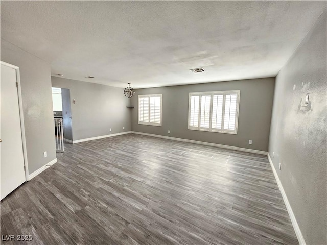 unfurnished room featuring visible vents, a textured ceiling, wood finished floors, a chandelier, and baseboards