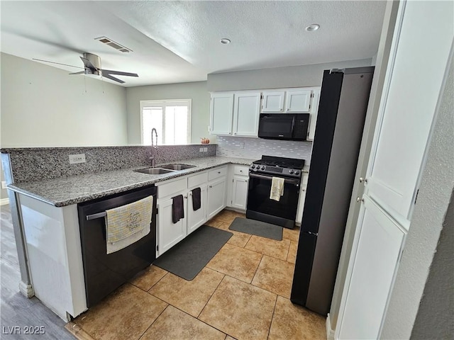 kitchen with white cabinets, a peninsula, light stone countertops, black appliances, and a sink