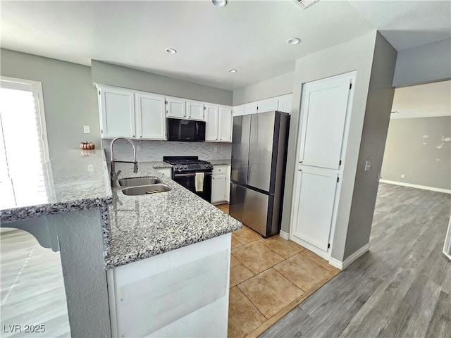 kitchen featuring white cabinets, a peninsula, light stone countertops, black appliances, and a sink