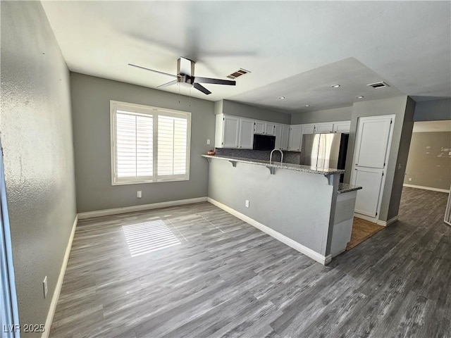 kitchen with black microwave, a peninsula, baseboards, freestanding refrigerator, and dark wood-style floors