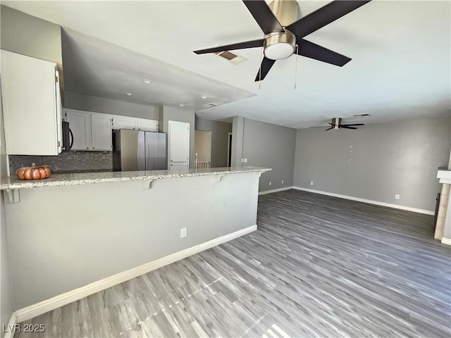 kitchen featuring baseboards, freestanding refrigerator, black microwave, a peninsula, and a kitchen breakfast bar