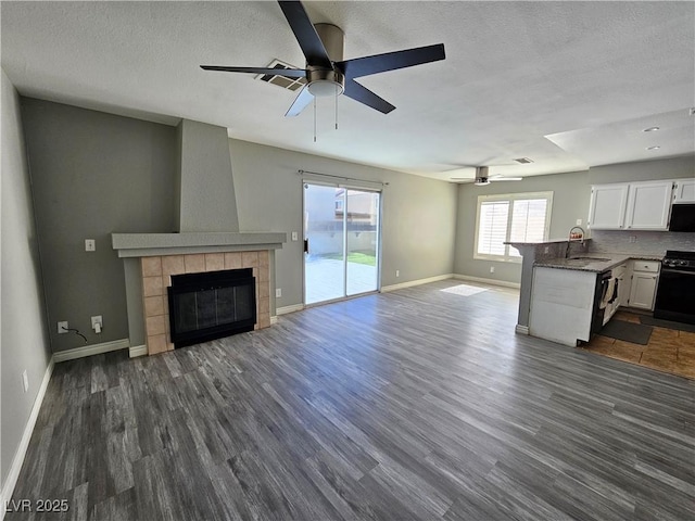 unfurnished living room featuring a sink, a tiled fireplace, baseboards, and dark wood-style flooring