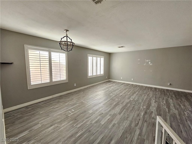 empty room with a textured ceiling, dark wood-type flooring, visible vents, baseboards, and an inviting chandelier