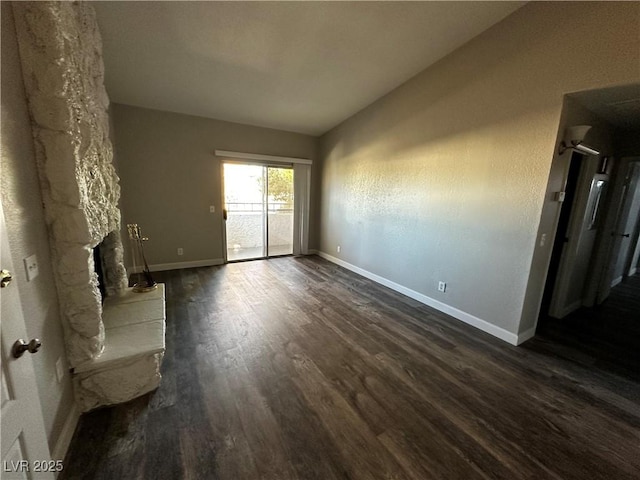 unfurnished living room featuring dark wood-style floors, baseboards, vaulted ceiling, and a stone fireplace