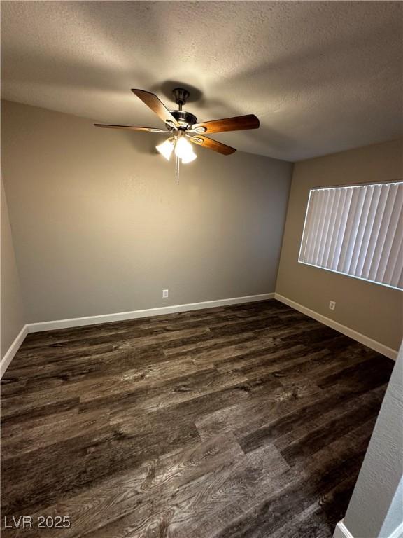 empty room featuring a textured ceiling, ceiling fan, dark wood finished floors, and baseboards