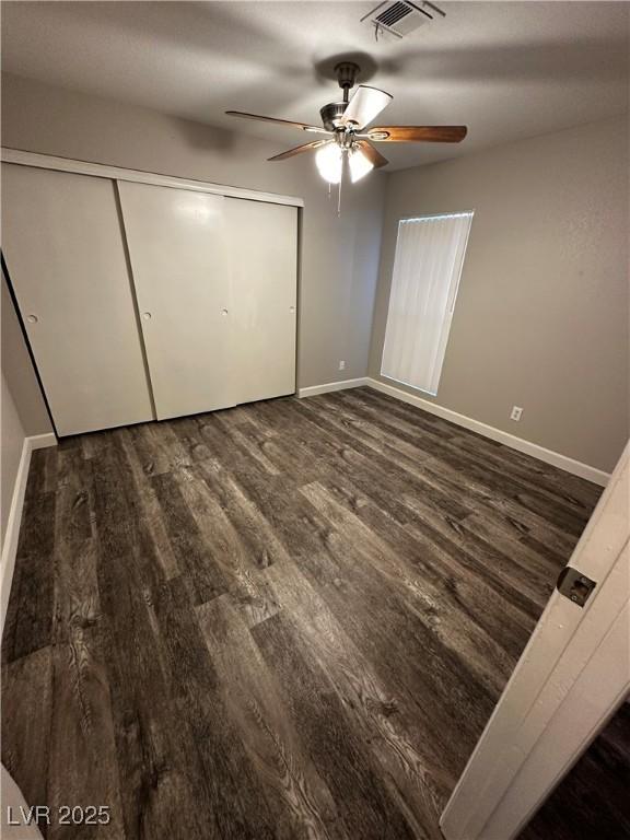 unfurnished bedroom featuring ceiling fan, dark wood-type flooring, visible vents, baseboards, and a closet