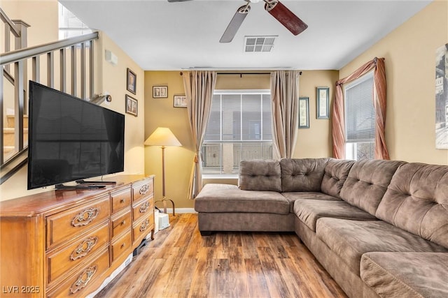 living area with visible vents, stairway, light wood-style floors, a ceiling fan, and baseboards