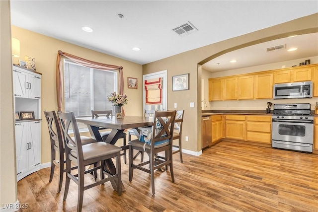 dining room featuring light wood-style floors, visible vents, arched walkways, and recessed lighting