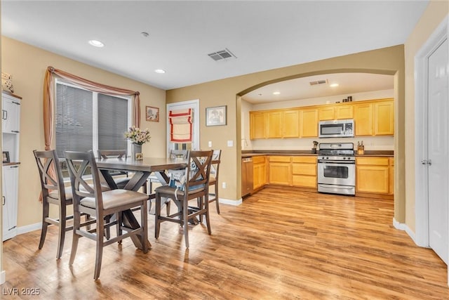 dining room with arched walkways, light wood-type flooring, visible vents, and recessed lighting