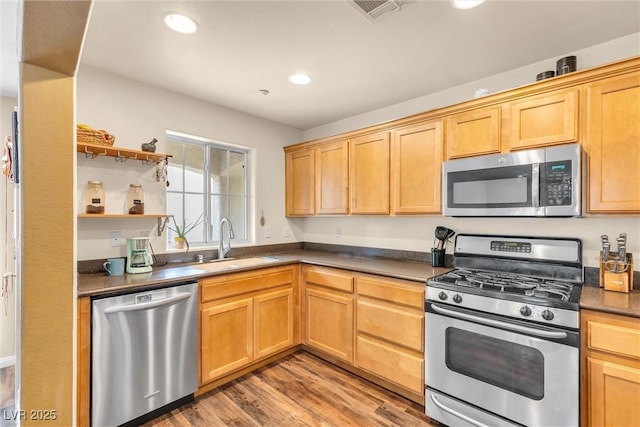 kitchen with stainless steel appliances, a sink, visible vents, light wood-style floors, and dark countertops