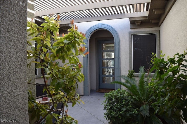 entrance to property featuring stucco siding and a pergola