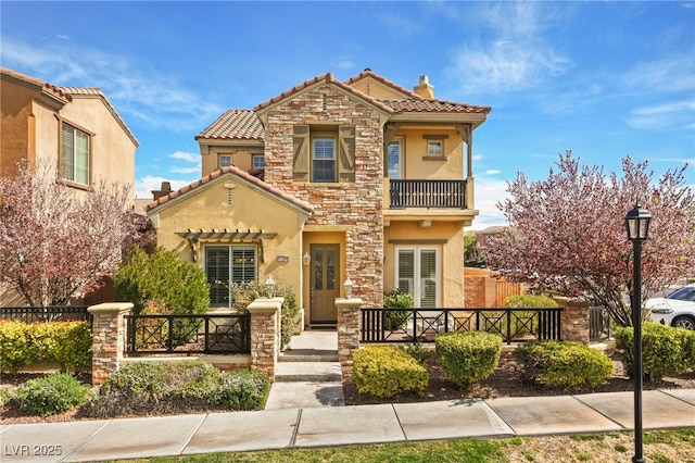 mediterranean / spanish house with stone siding, stucco siding, a balcony, and fence