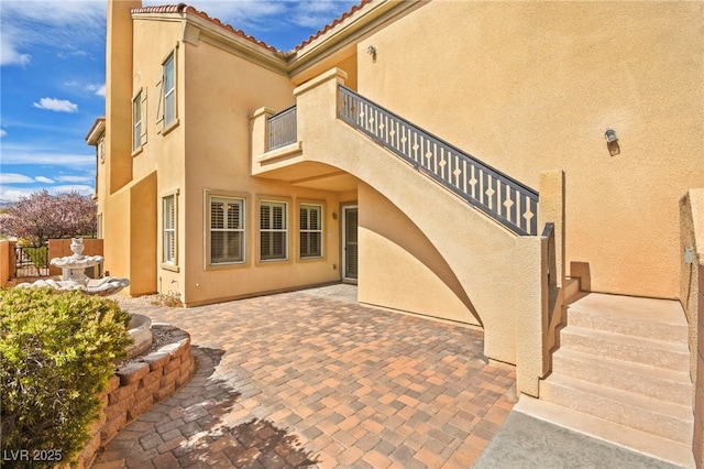 exterior space featuring a balcony, a tiled roof, a patio area, and stucco siding