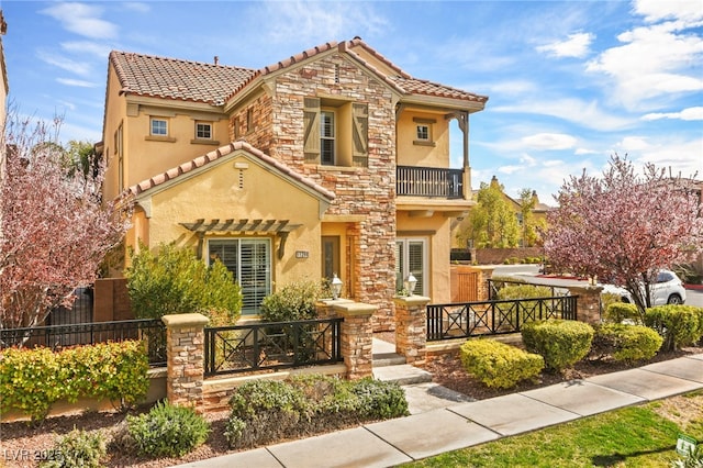 mediterranean / spanish-style home with a balcony, fence, stucco siding, stone siding, and a tile roof