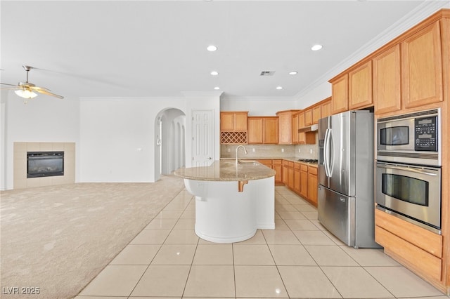 kitchen featuring arched walkways, a sink, stainless steel appliances, light carpet, and open floor plan