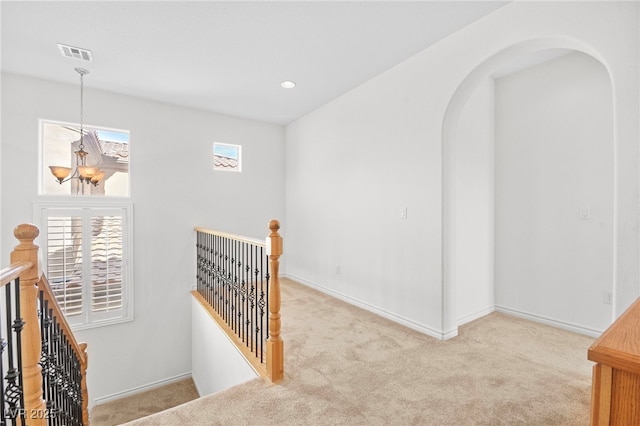 corridor with an upstairs landing, visible vents, a notable chandelier, and carpet