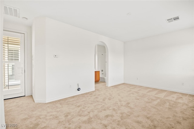 spare room featuring arched walkways, visible vents, light colored carpet, and baseboards