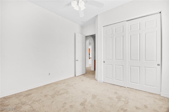 unfurnished bedroom with a ceiling fan, a closet, arched walkways, carpet flooring, and baseboards