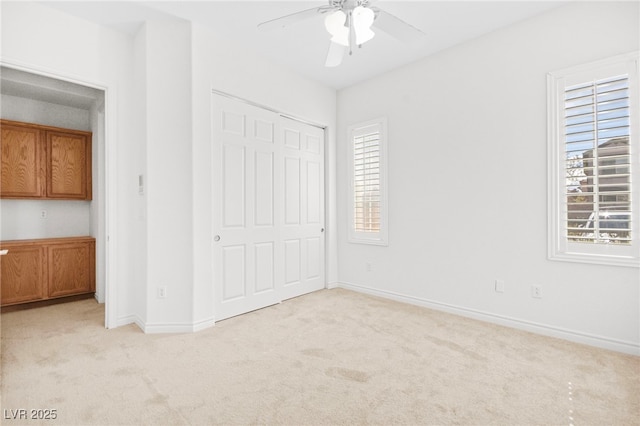 unfurnished bedroom featuring a closet, baseboards, light colored carpet, and ceiling fan