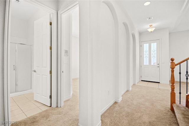 hall with stairway, light colored carpet, visible vents, and arched walkways