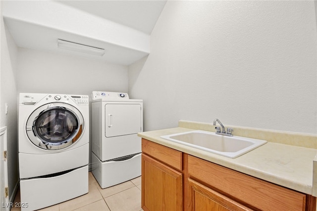 laundry area featuring washing machine and clothes dryer, light tile patterned floors, cabinet space, and a sink