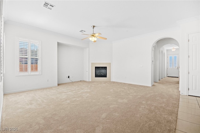 unfurnished living room featuring visible vents, ornamental molding, a tiled fireplace, light colored carpet, and ceiling fan