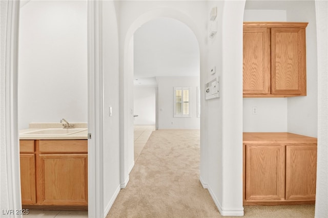 hallway featuring light carpet, arched walkways, and a sink