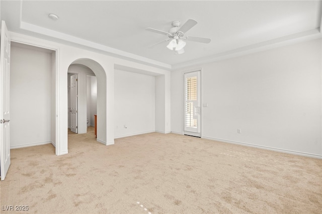 empty room with ceiling fan, baseboards, arched walkways, and light carpet