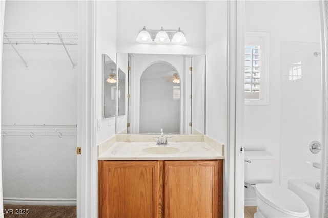 full bathroom featuring a spacious closet, toilet, vanity, and ceiling fan