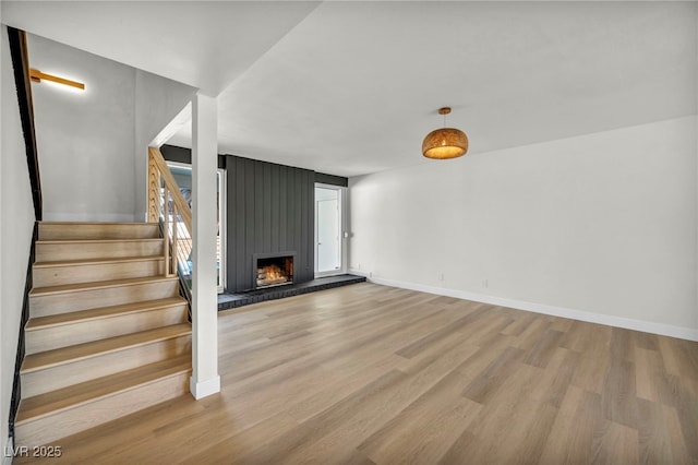 unfurnished living room featuring stairway, a large fireplace, baseboards, and wood finished floors