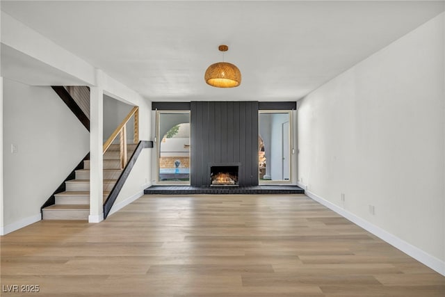 unfurnished living room with stairway, wood finished floors, baseboards, and a large fireplace