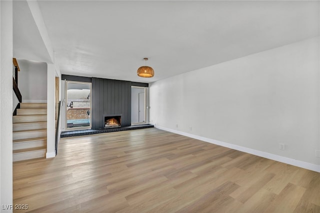 unfurnished living room with light wood-type flooring, a large fireplace, baseboards, and stairs