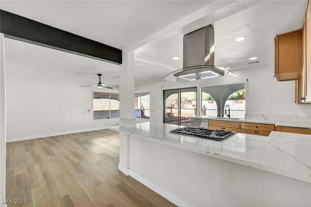 kitchen with beamed ceiling, light wood-style flooring, a sink, gas stovetop, and island range hood