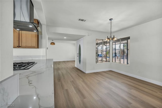 unfurnished dining area with visible vents, baseboards, a chandelier, and light wood finished floors