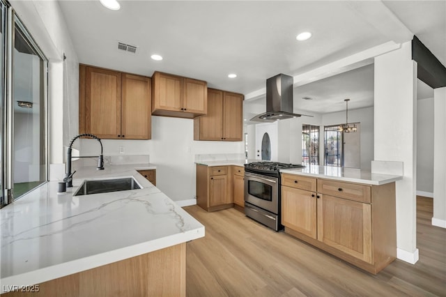 kitchen with light stone counters, a sink, light wood-style floors, gas range, and island range hood