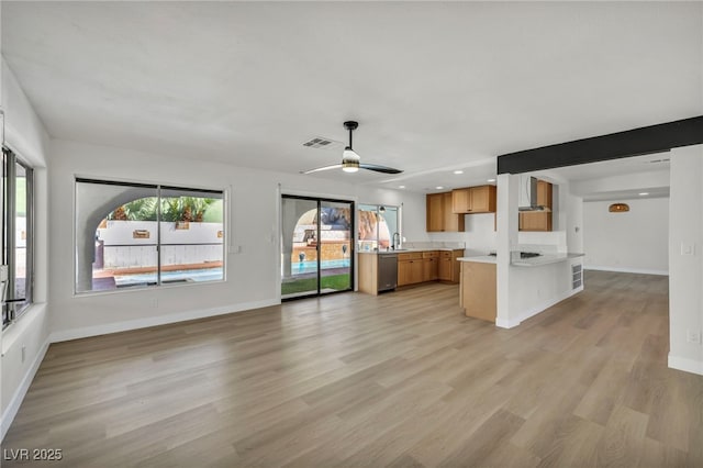 kitchen featuring visible vents, wall chimney range hood, light countertops, light wood-style floors, and brown cabinetry