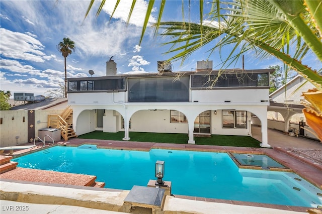 rear view of house featuring a pool with connected hot tub, stairway, a sunroom, a chimney, and a patio area