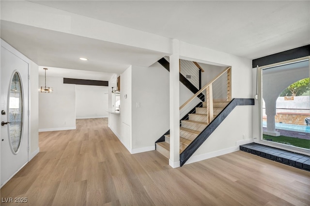 foyer entrance with stairway, baseboards, light wood-style floors, and a chandelier