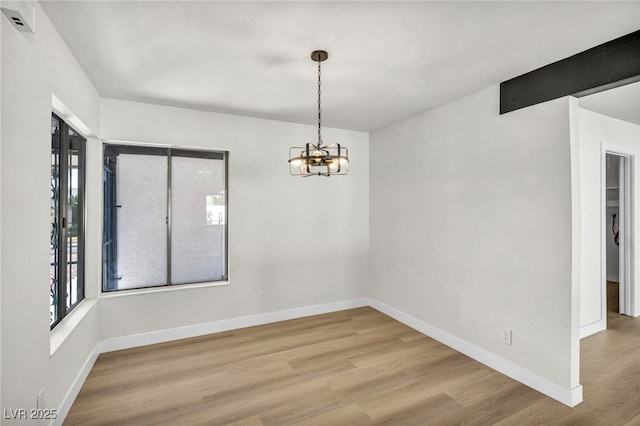 spare room featuring a notable chandelier, a healthy amount of sunlight, baseboards, and wood finished floors