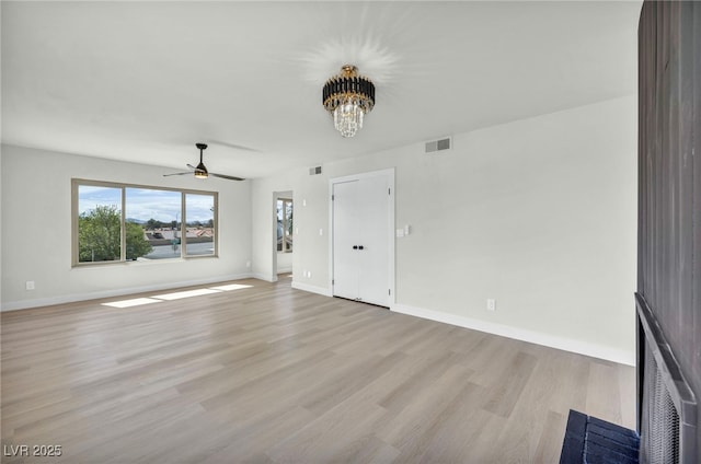 unfurnished living room featuring visible vents, baseboards, a fireplace, light wood-style floors, and ceiling fan with notable chandelier