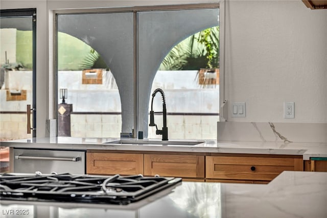 kitchen with brown cabinetry, light stone countertops, a sink, stove, and dishwasher