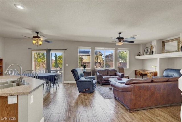 living room with a textured ceiling, a ceiling fan, light wood-style floors, and a healthy amount of sunlight