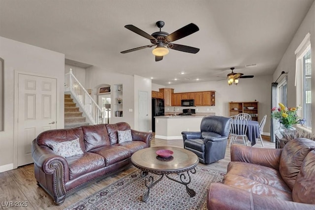 living room featuring stairway, baseboards, light wood-style floors, and a healthy amount of sunlight