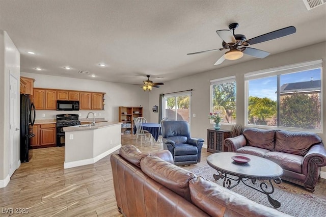 living area with visible vents, light wood-type flooring, recessed lighting, a textured ceiling, and a ceiling fan