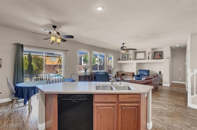 kitchen with a center island with sink, light wood finished floors, a sink, light countertops, and black dishwasher