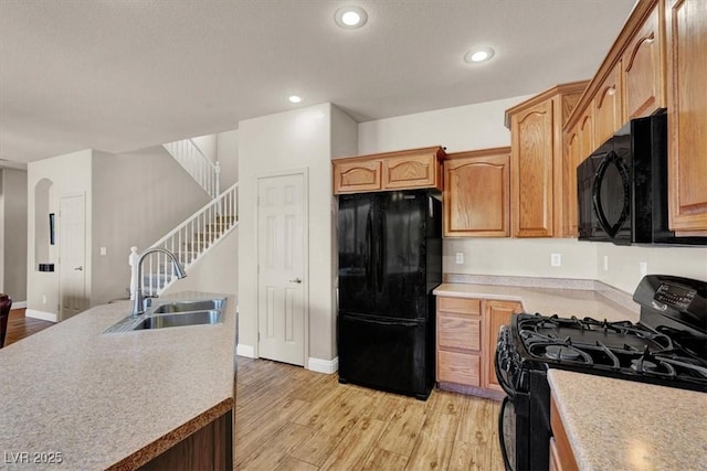 kitchen with light wood finished floors, recessed lighting, a sink, black appliances, and light countertops