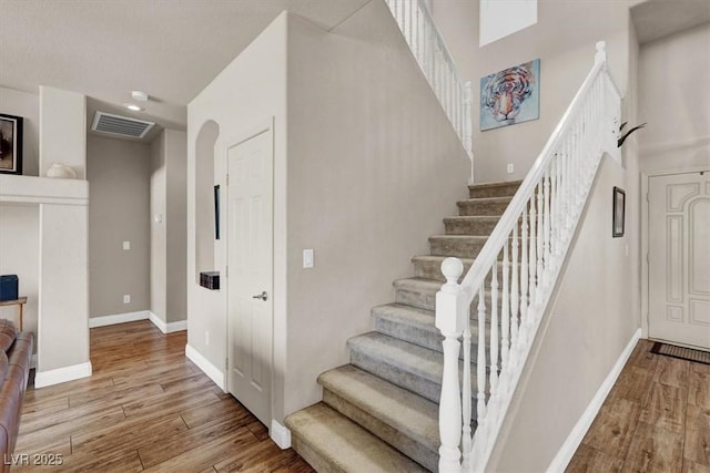 stairway featuring visible vents, baseboards, arched walkways, and wood finished floors